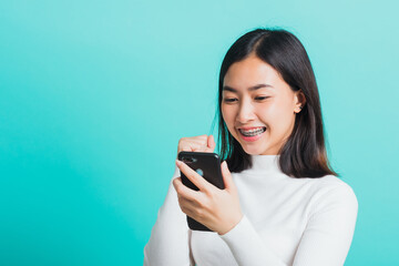 Asian woman smile holding smartphone she happy and surprised after received message, female excited cheerful her reading mobile phone some social media isolated on blue background, Technology concept
