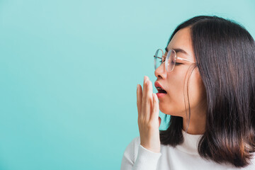 Portrait female bored yawning tired covering mouth with hand, Young beautiful Asian woman sleepy covering opened mouth with palm, studio shot isolated on a blue background