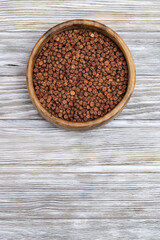 Raw gray peas in round wooden bowl on light wood. Organic healthy diet food. Vertical format image with copy space.