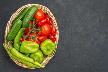 Fresh vegetables red tomatoes with stems green peppers and cucumbers necessary for cooking on dark...