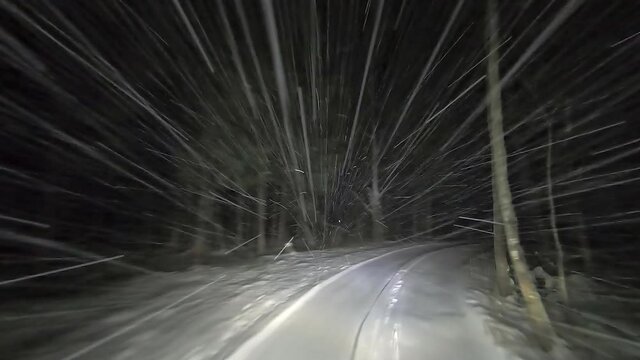 Drive by car at night on a winter forest road in snowfall. Heavy snow is reflected in the light of the car headlights. Travel in winter by car