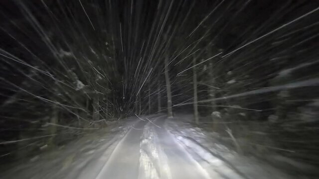 Drive by car at night on a winter forest road in snowfall. Heavy snow is reflected in the light of the car headlights. Travel in winter by car