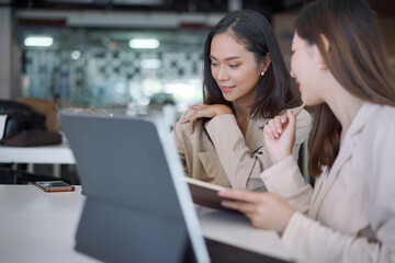 Fototapeta premium Two young asian women colleagues in smart casual wear planning business strategy together at the modern coworking space.
