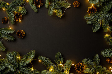 garland of fir branches and cones and lights on a black background with copy space