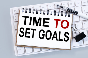 TIME TO SET GOALS, text on white notepad paper on white keyboard on gray background