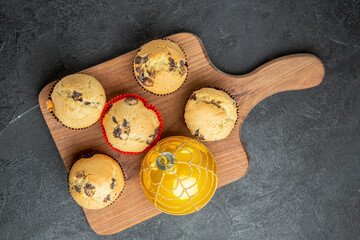 Above view of freshly baked delicious small cupcakes with chocolates and accessory on wooden cutting board on dark background