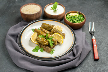 bottom close view bowls with natural yogurt parsley rice dolma in grape leaves on white plate a fork a purple kitchen towel on dark background