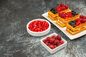 bottom view berry waffles on white rectangular plate bowls of pomegranate and raspberries on grey-white background with copy space