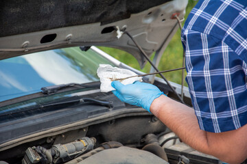A man in a blue shirt and gloves checks the oil level in the car.