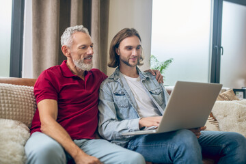 Two men sitting next to each other and watching something on laptop