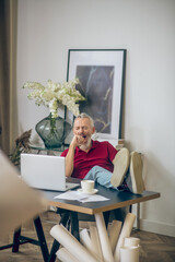 Grey-haired man sitting at the laptop and looking bored