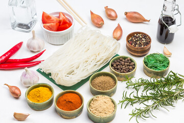 Rice noodles and dry spices in green small bowls. Onions, rosemary sprigs and bamboo sticks. Soy sauce in glass bottle