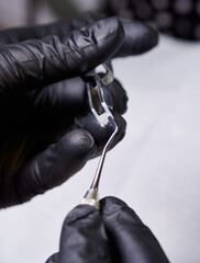 Macro shooting of orthodontic ceramic bracket in dentist's hands wearing black latex gloves. Process of putting adhesive paste on bracket before installation. Orthodontic accessories concept