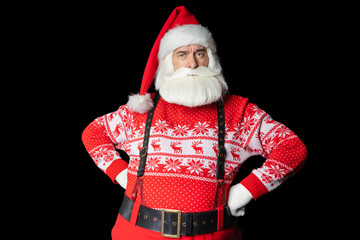 Senior man of frowning Santa Claus standing with hands on hips while posing against black background in studio, copy space. Isolated black background.