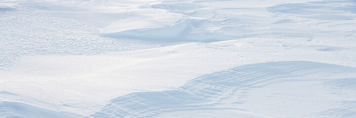 Beautiful winter background with snowy ground. Natural snow texture. Wind sculpted patterns on snow surface. Arctic, Polar region.