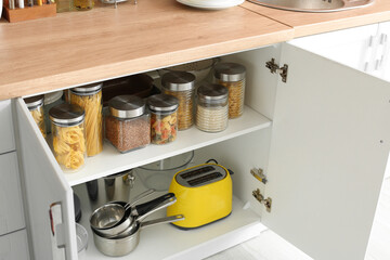 Shelves with kitchenware and glass jars with products in cupboard