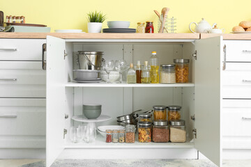 Shelves with utensils and glass jars with products in cupboard - obrazy, fototapety, plakaty