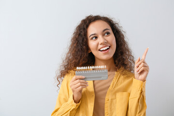 Beautiful young woman with teeth samples showing something on light background
