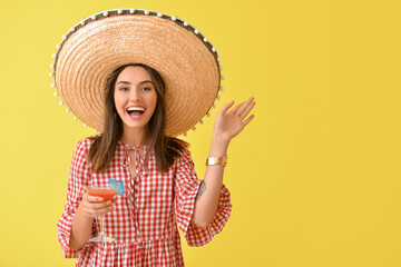 Beautiful Mexican woman in sombrero hat and with cocktail on color background