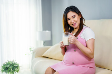 Obraz na płótnie Canvas pregnant woman drinking a glass of milk on sofa in living room