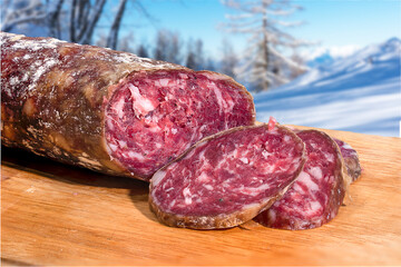 salami in the foreground on a wooden cutting board with some bread cookies - mountain landscape...