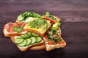 Toasts, sandwiches with cream cheese, cucumbers, tomatoes, salmon, sprouts, egg on a brown wooden background. close-up Healthy food concept.