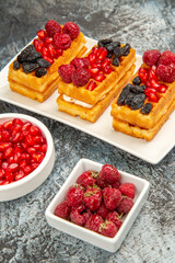 bottom view berry waffles on white rectangular plate bowls of pomegranate and raspberries on grey-white background