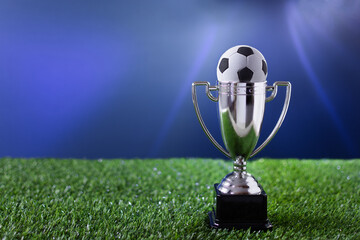 Soccer championship silver cup on a grass over blue background.
