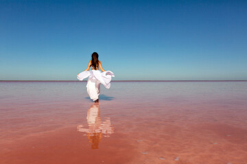 Beautiful woman in a white dress on a pink lake on a summer sunny day