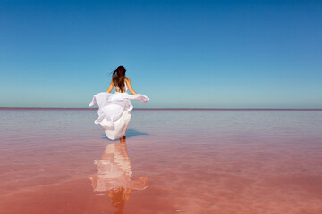 Beautiful woman in a white dress on a pink lake on a summer sunny day
