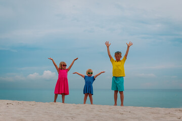 happy kids enjoy beach vacation, boy and girl hands up at sea