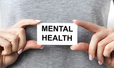The girl holds a card with the text of Mental Health, the background is gray.