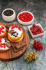 top view berry cakes and chocolates on chopping board xmas toys bowls with pomegranate raisins and raspberries on grey-white background