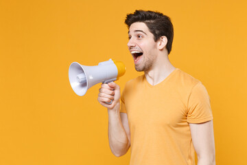 Young unshaved surprised happy student man 20s wearing casual basic t-shirt screaming in megaphone announces discounts sale hurry up looking aside isolated on yellow color background studio portrait.