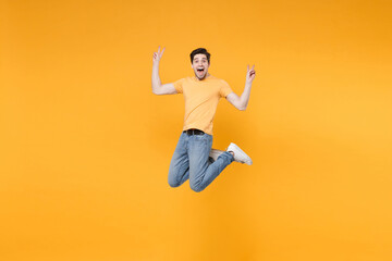 Fototapeta na wymiar Full length of young overjoyed happy caucasian excited fun man 20s wearing casual basic t-shirt jeans high jumping up showing victory sign gesture isolated on yellow color background studio portrait.