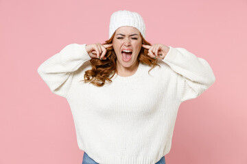 Crazy frustrated young redhead plus size body positive woman 20s in basic warm white sweater hat covering ears with fingers keeping eyes closed screaming isolated on pink background studio portrait.