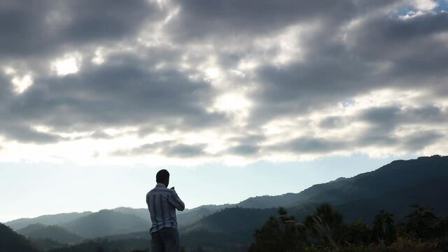 A man standing praying on a mountaintop.