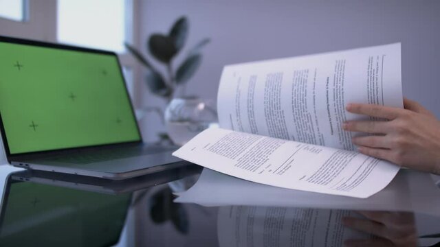 Female hands flipping through document, in front of chromakey screen laptop.