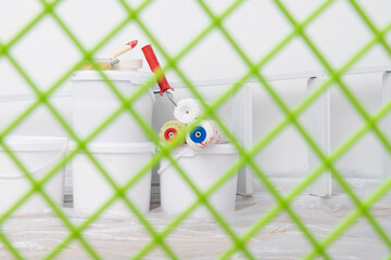 through the green grid view of the paint buckets and tools against the white wall