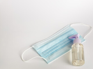 White background with a bottle of hand sanitizer and a bunch of disposal face mask. Selective focus.Medical concept.