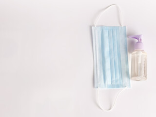 White background with a bottle of hand sanitizer and a bunch of disposal face mask. Selective focus.Medical concept.