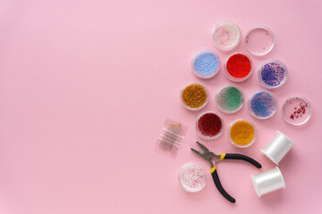 Flat lay of items for creativity. Beads, fishing line and wire cutters on pink background, copyspace