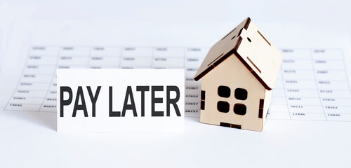 Closeup of house wooden model with blank for text PAY LATER on chart background.
