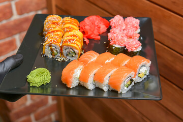 Waiter with plate of sushi, against the brown brick background. Restaurant service, waiter at work.