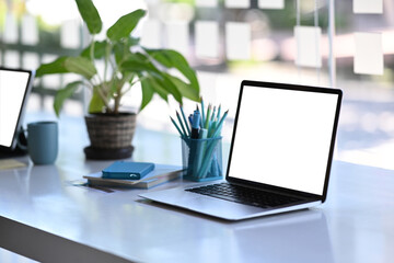 Fototapeta premium Freelancer or designer workspace with a laptop computer with blank screen, stationery and notebook on white table.