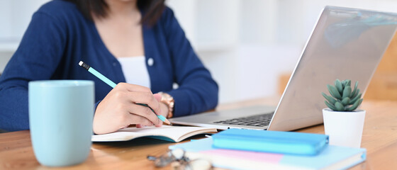 Young woman college student using laptop computer studying online from home and making notes on notebook.
