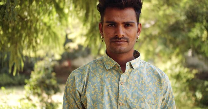 Slow-motion static close-up portrait of a young adult Indian man outdoors staring looking at camera pov with confident expressionless 