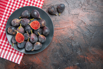 Above view of full fresh black mission figs split ones on a black plate on red stripped towel on colorful table