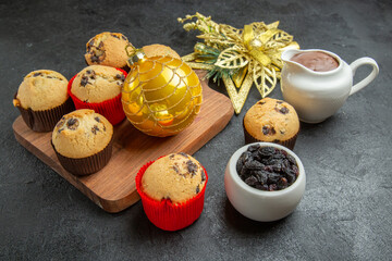 Tea break with delicious small cupcakes with chocolates served with decorations on wooden board on dark background