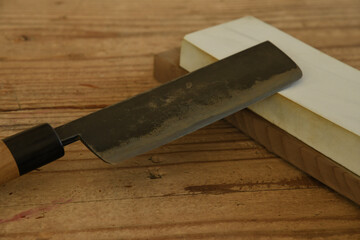 Kitchen knife and whetstone on wooden board.